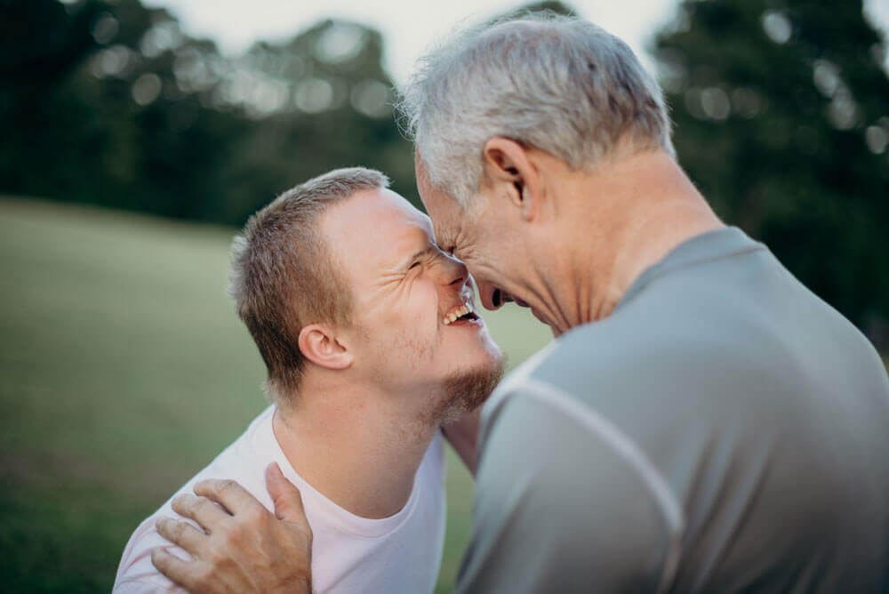 An old man and a young man with a disability smile at each other 