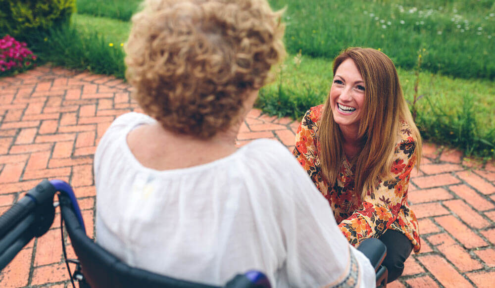 a young woman smiles at an older woman in a wheelchair