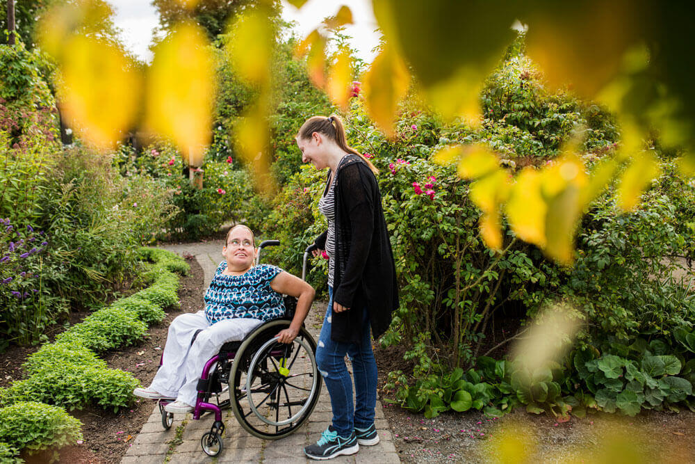 A person in a wheelchair in a garden with another person