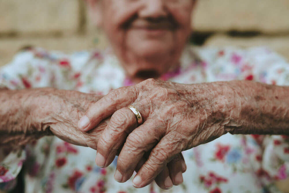 An older woman clasps her hands 